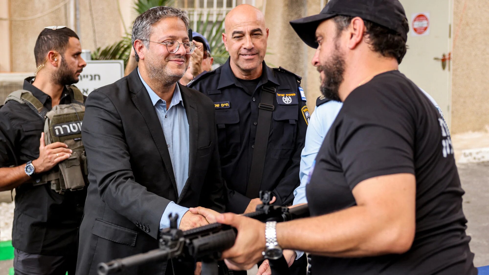 Israel's National Security Minister Itamar Ben-Gvir shakes hands with a volunteer of the new civilian guard unit while handing out M5 automatic assault riflesin Ashkelon on 27 October 2023 (AFP/Menahem Kahana)