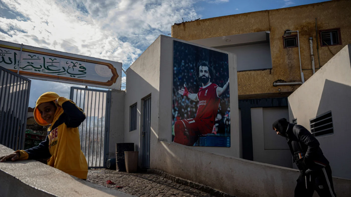 Egyptians walk past a picture of Liverpool's footballer Mohamed Salah at his Youth Centre in the Egyptian village of Nagrig, about 120km northwest of Cairo on 10 December 2025 (Khaled Desouki/ AFP)