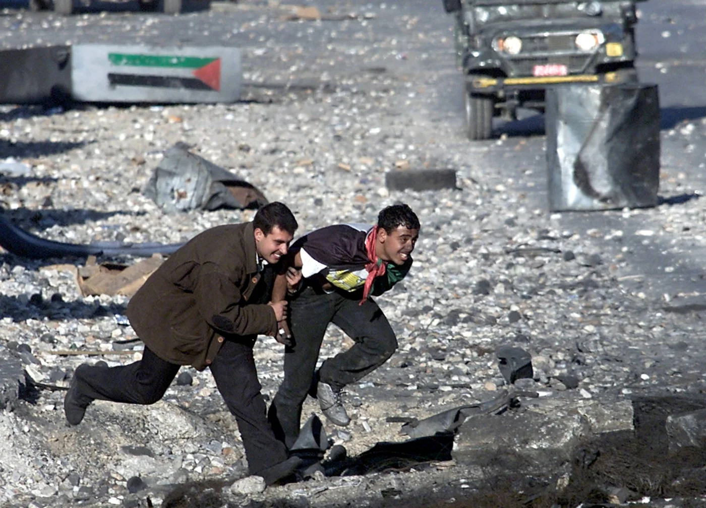 A wounded Palestinian and his friend run for cover from Israeli soldiers in Ramallah, West Bank in November 2000 during the Second Intifada (AFP)